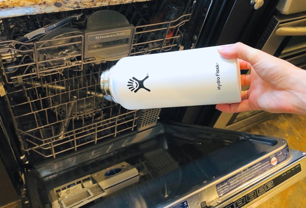 how to clean water bottles hand holding a white hydroflask water bottle over open dishwasher 