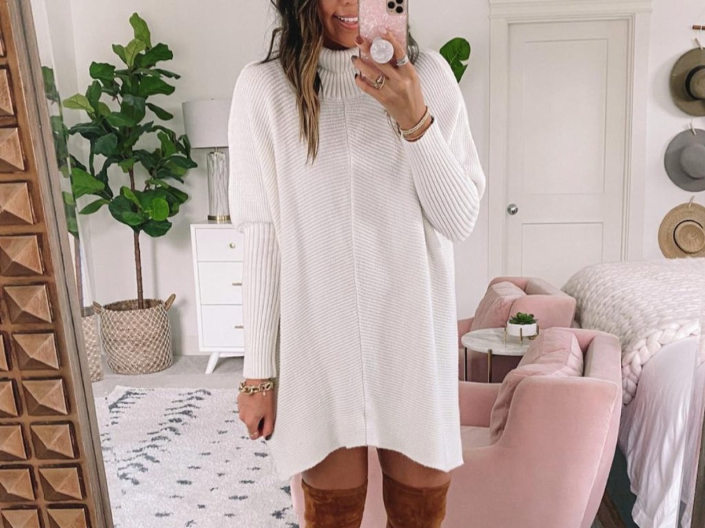 woman taking selfie in white sweater and high boots