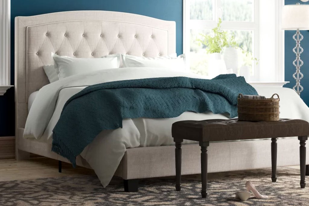 cream colored tuffed upholstered headboard and bed frame with mattress and white and blue bedding