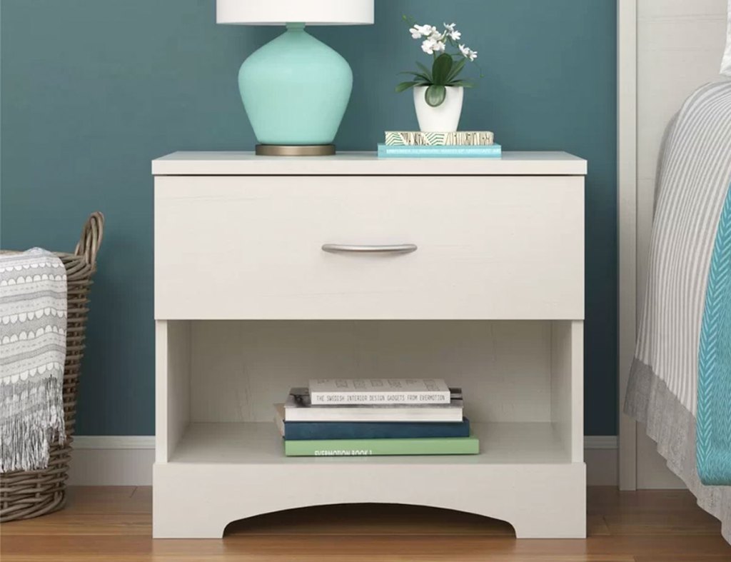 white one drawer nightstand with books and lamp on top