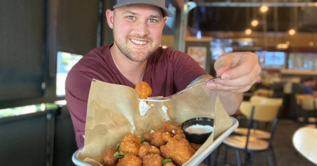 man holding up plate of cauliflower wings in one hand and fork with cauliflower wing in other hand