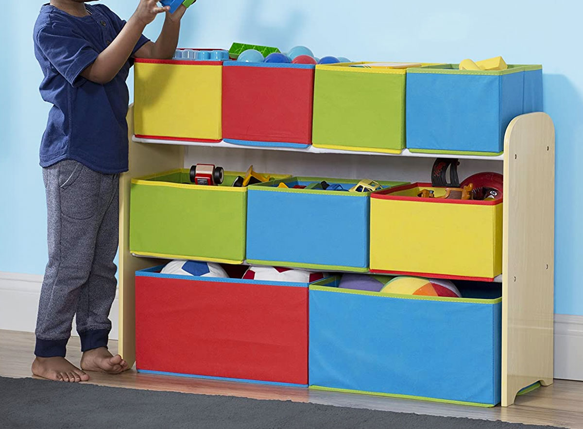 boy standing next toy organizer with nine colorful fabric bins