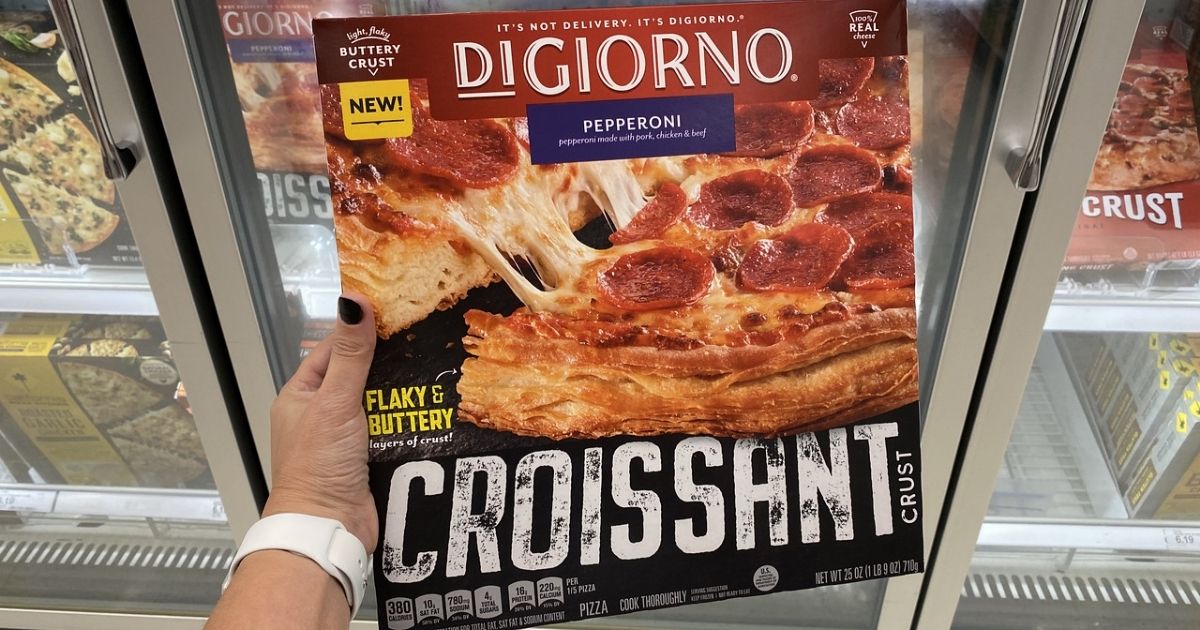 hand holding the New Digiorno Croissant Crust Pizza box in front of a store freezer case