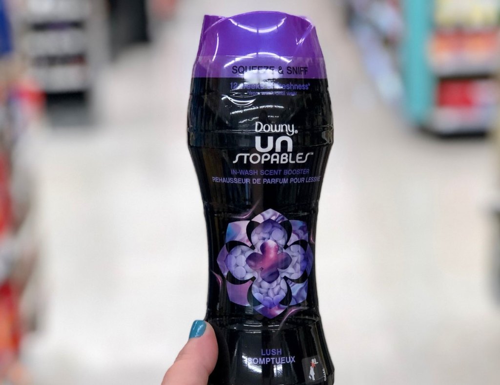 person holding up black and purple bottle of downy unstoppables laundry scent beads