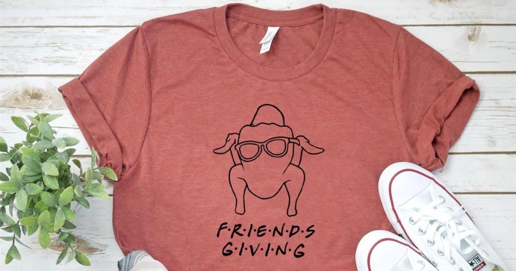 red Friendsgiving tee on wood surface, plant, white sneakers
