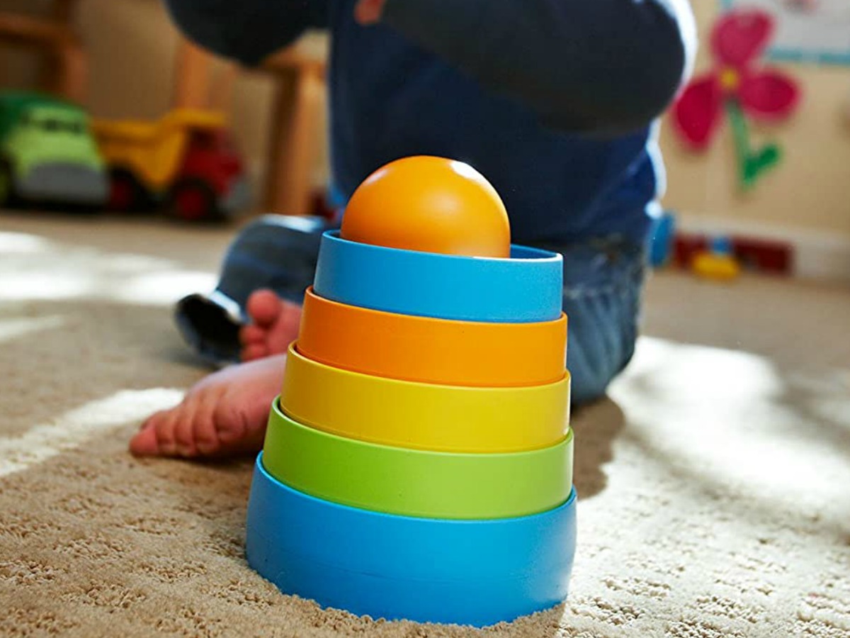 Baby playing with a colorful stacker toy on a carpeted floor