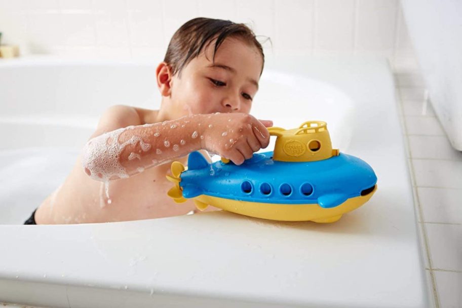 boy in bubble bath with green toy blue and yellow submarine ship