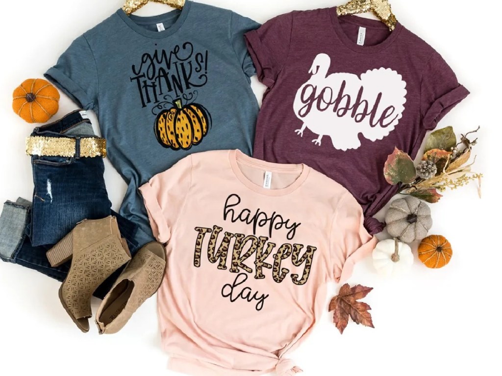 three Thanksgiving tees, jeans, boots, and pumpkins