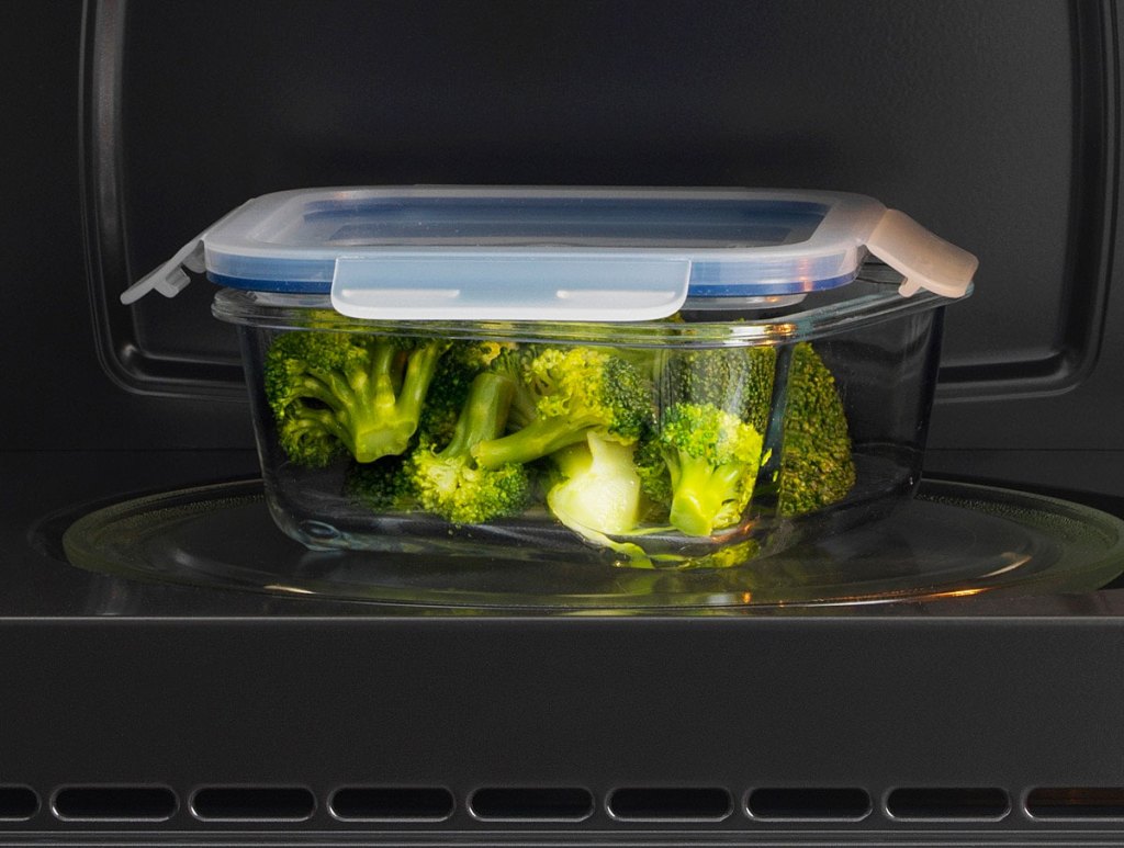 glass food storage container filled with broccoli in black microwave