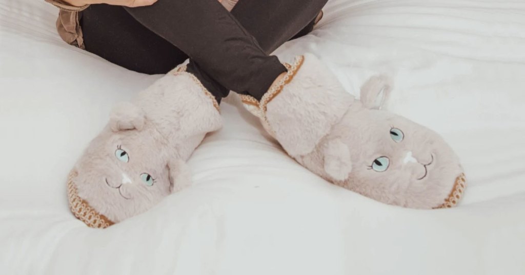 woman sitting on bed wearing a pair of cat shaped fuzzy slippers