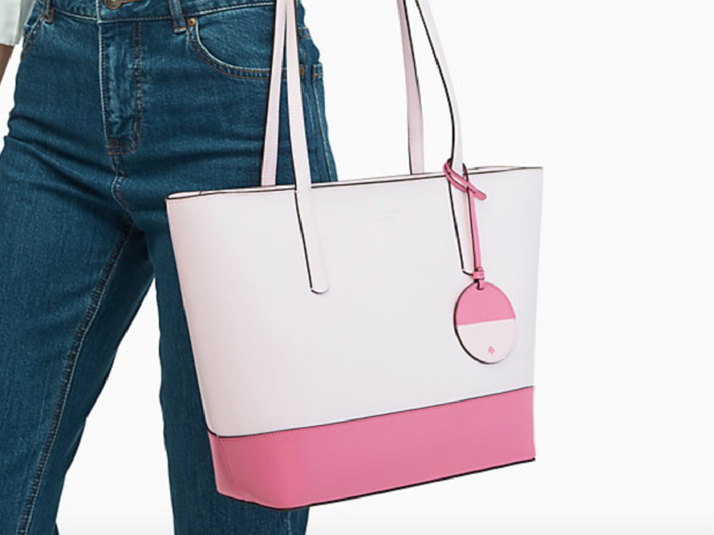 Woman wearing a white top and blue jeans holding a large pink and cream Kate Spade Tote