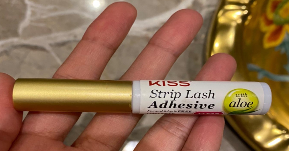 Kiss strip lash adhesive. White tube with gold top. A left hand is holding it.