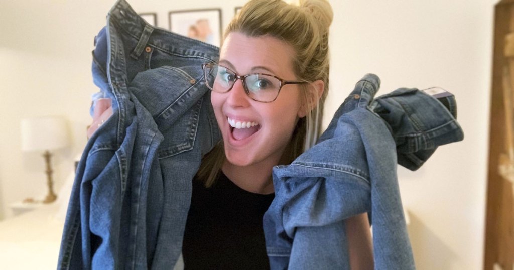 woman with blonde hair and glasses holding up multiple pairs of jeans