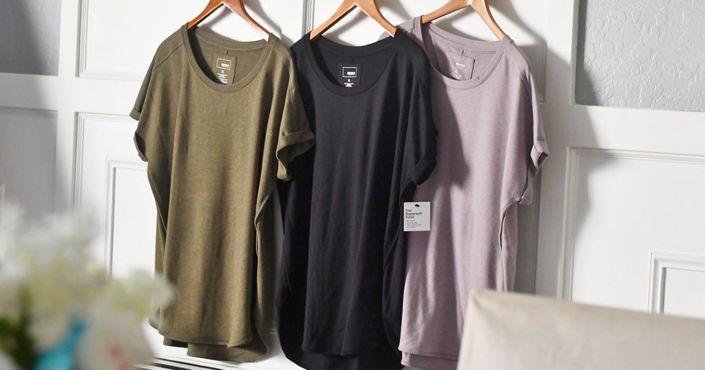 olive green, black, and mauve colored tunic tops hanging on wooden hangers
