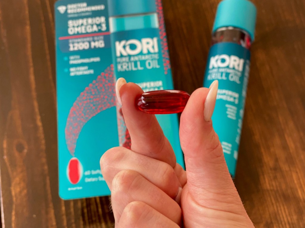 Woman holding up 1 red capsule of Krill Oil