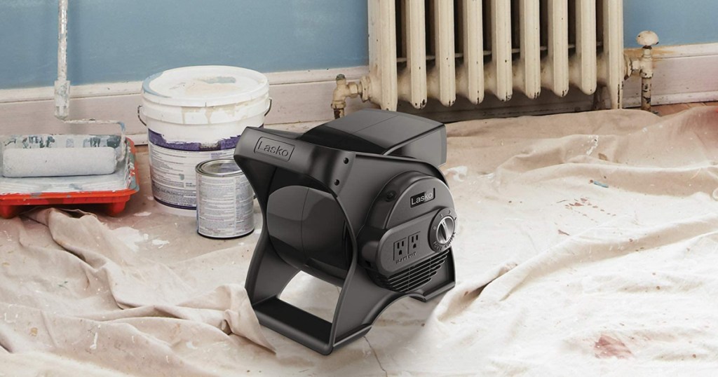 Lasko Pivoting Fan sitting on a drop cloth next to paint buckets and a radiator
