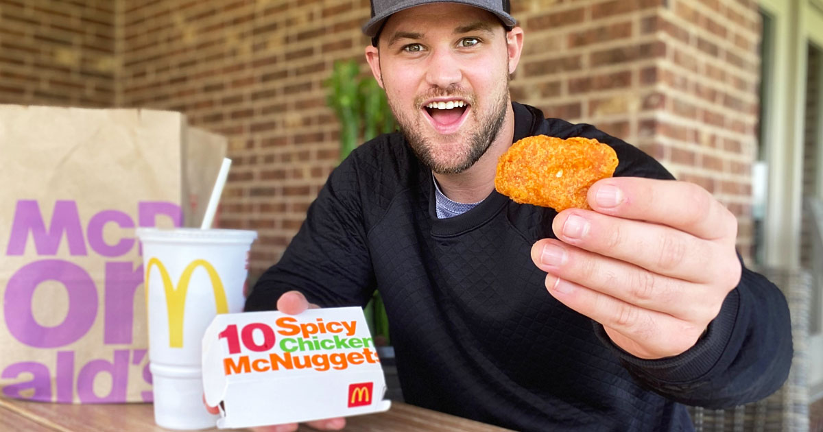 man in black hoodie holding up box of McDonals spicy chicken nuggets in one hand and single chicken nugget in other hand