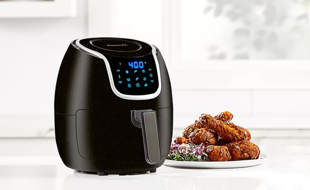 black air fryer with blue digital touch screen on white countertop with plate of chicken wings