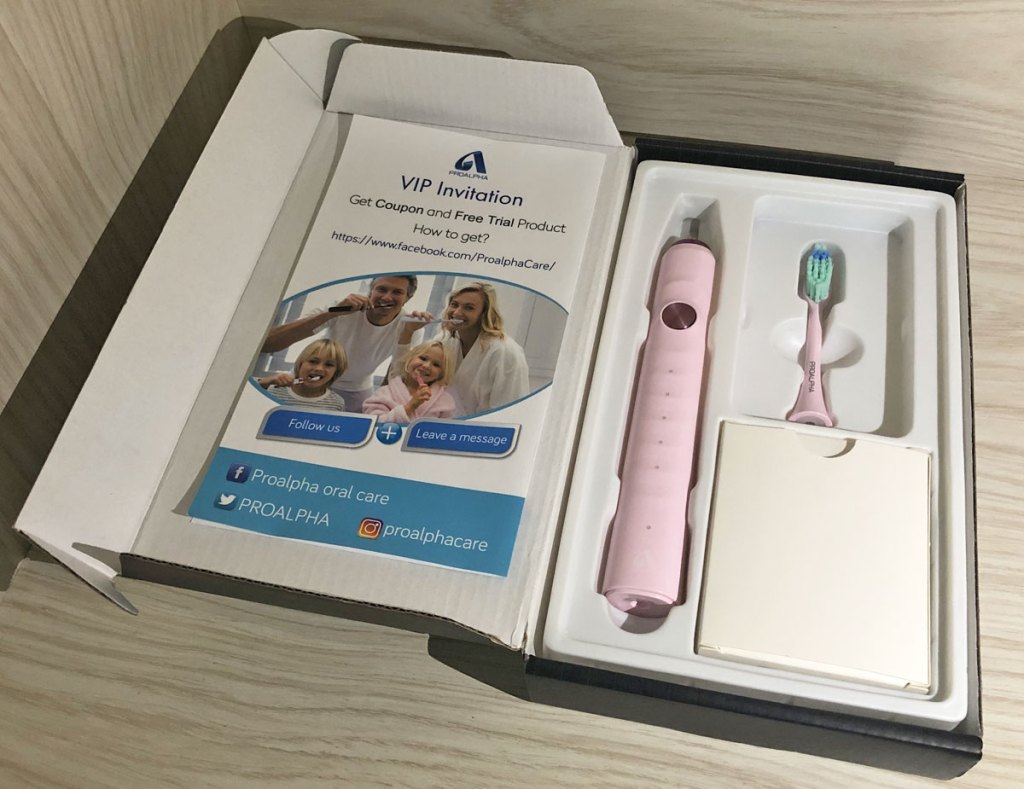 light pink electric toothbrush inside it's box with accessories and instructions