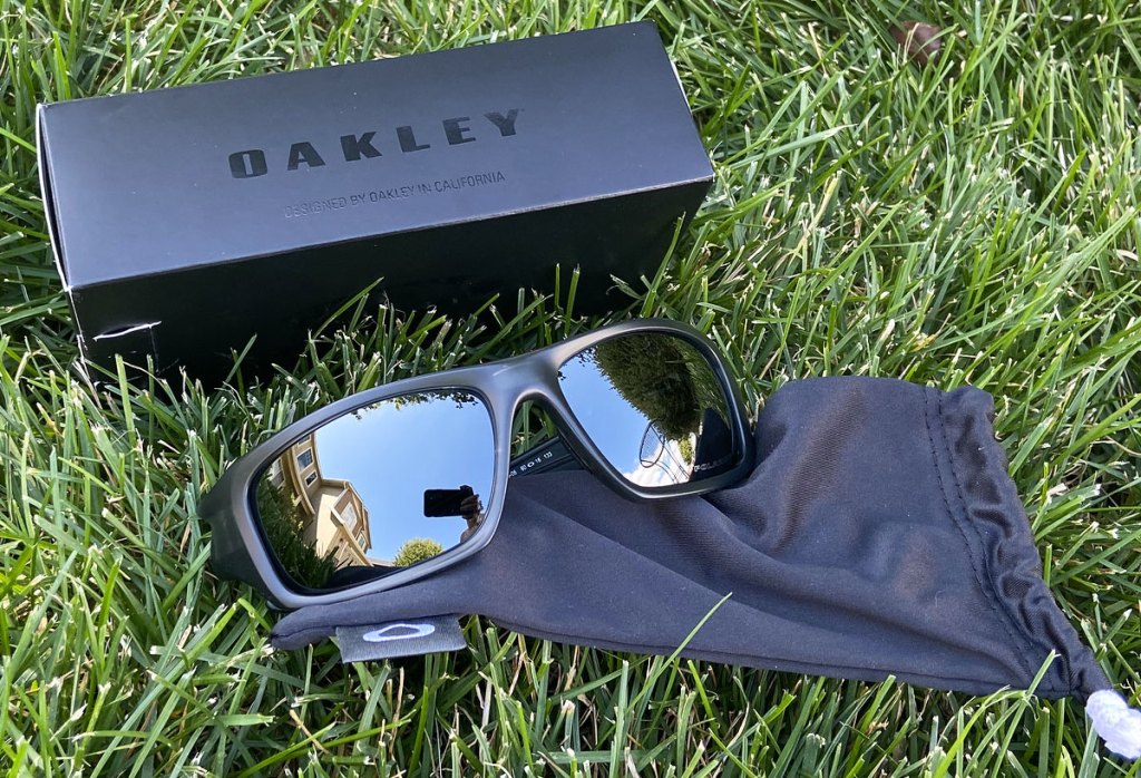 pair of black oakley sunglasses laying in grass near to storage bag and box