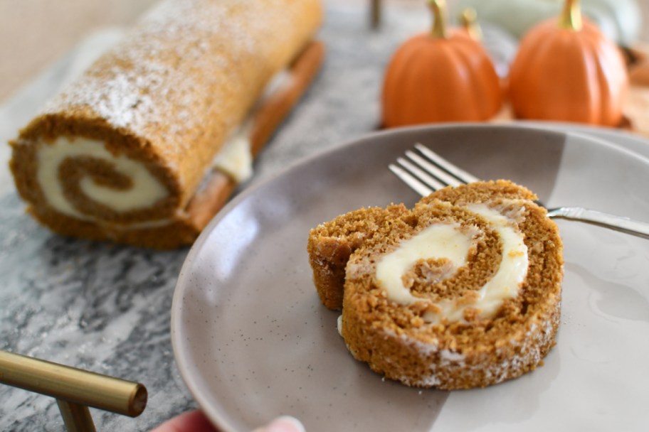 A pumpkin Swiss roll on a plate next to fall decor