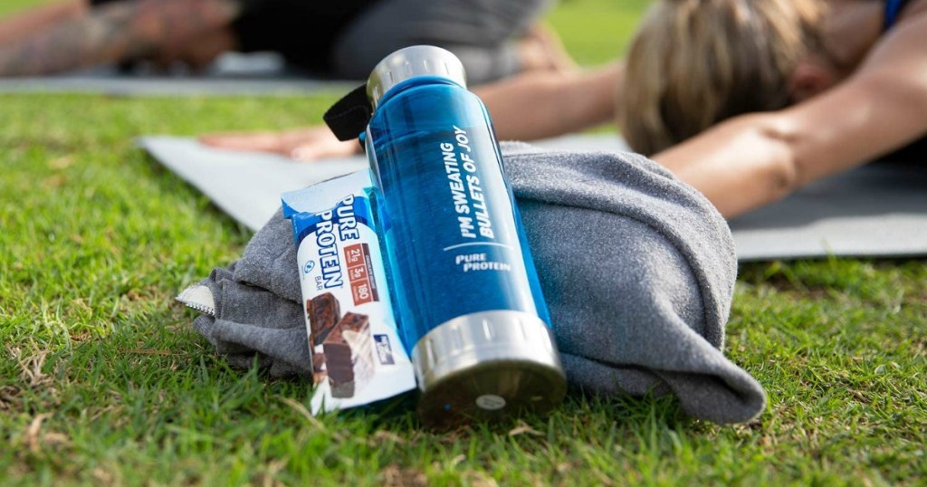 Protein bar and water bottle in the grass near a woman stretching