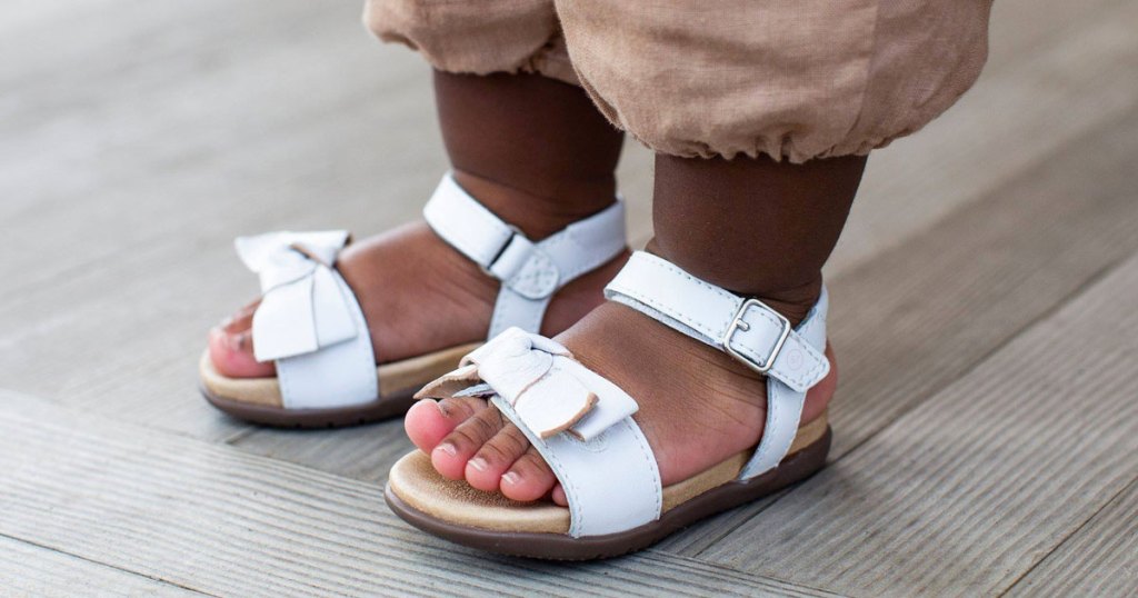toddler girl wearing a pair of white leather sandals with matching bows on tops