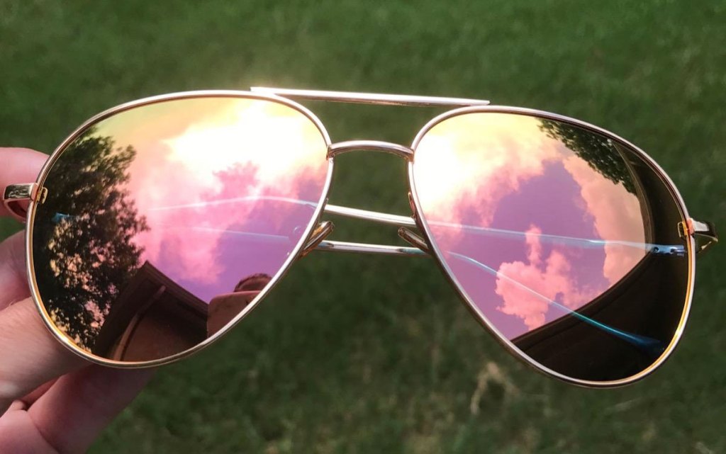 person holding pair of aviator sunglasses with gold frames and pink mirrored lenses