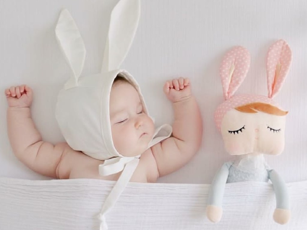 baby wearing bunny ears sleeping next to a stuffed sweet dreams doll