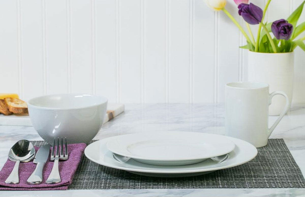 round white dinnerware set on table with silverware and vase of flowers