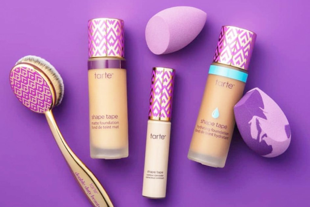 bottles of Tarte shape tape concealer and foundation with brush and sponges on a purple background