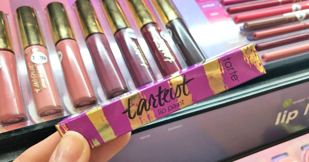person holding up a Tarte lip paint box in front of display of different shades