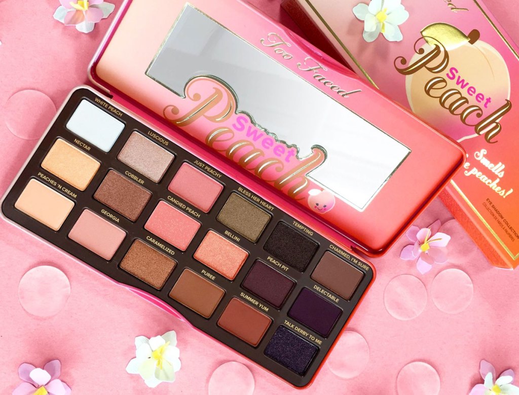 too faced sweet peach eyeshadow palette on pink background with flowers around it