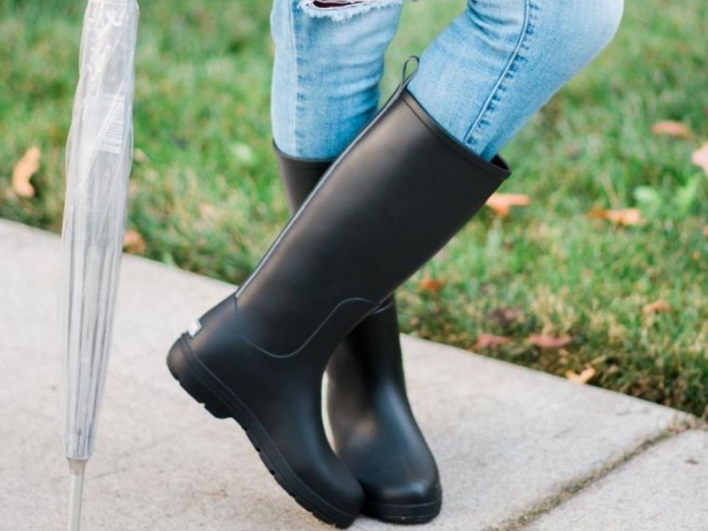 woman wearing tall rain boots with jeans and holding an umbrella 