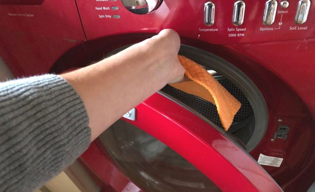 A hand placing a cloth in the washing machine