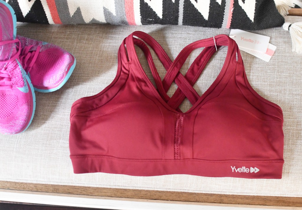 maroon colored criss-cross sports bra on grey bench with pink running shoes next to it