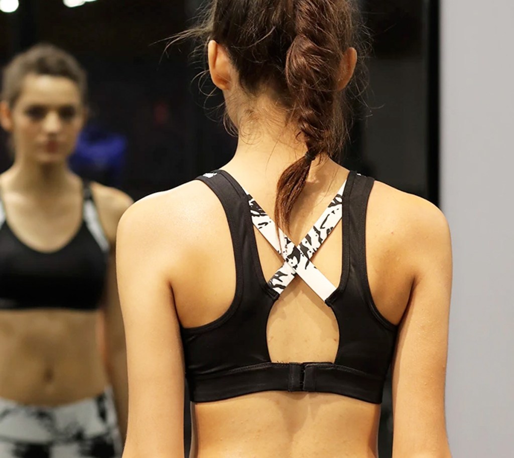 woman stanind in mirror wearing a black sports bra with white criss-crossing back straps