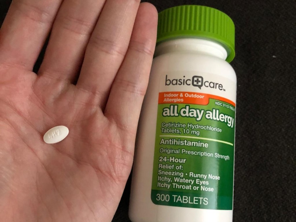 holding a white pill next to a bottle of antihistamines