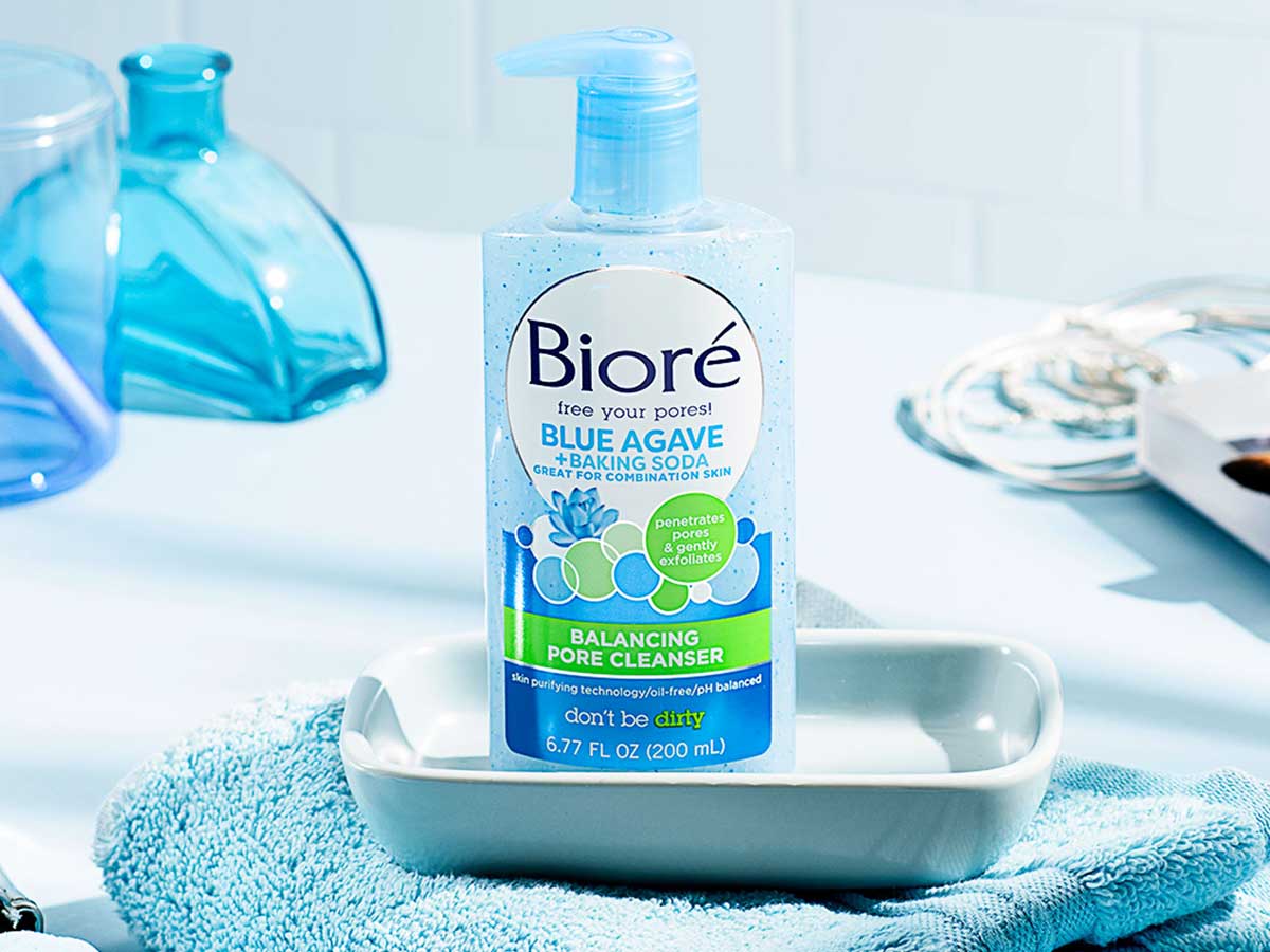 light blue bottle of face wash in a soap dish on a towel on a bathroom counter near blue containers