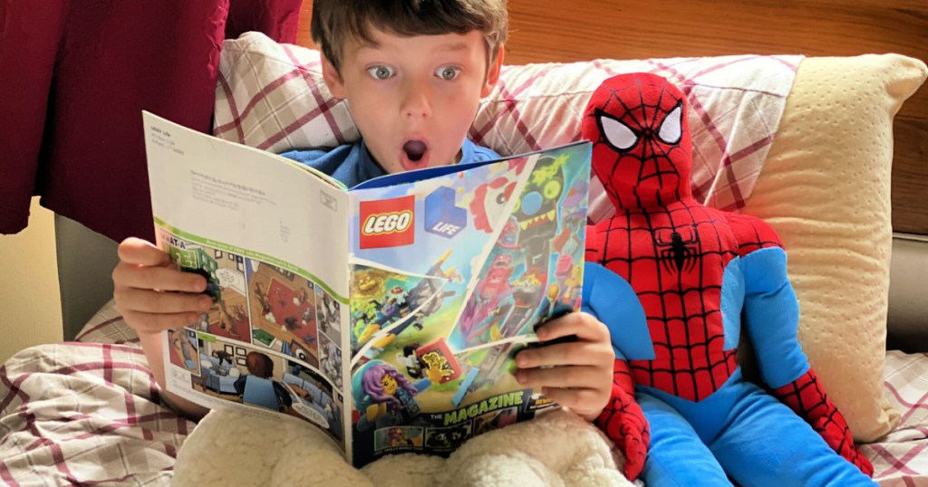 boy reading a lego magazine on his bed with spiderman plush