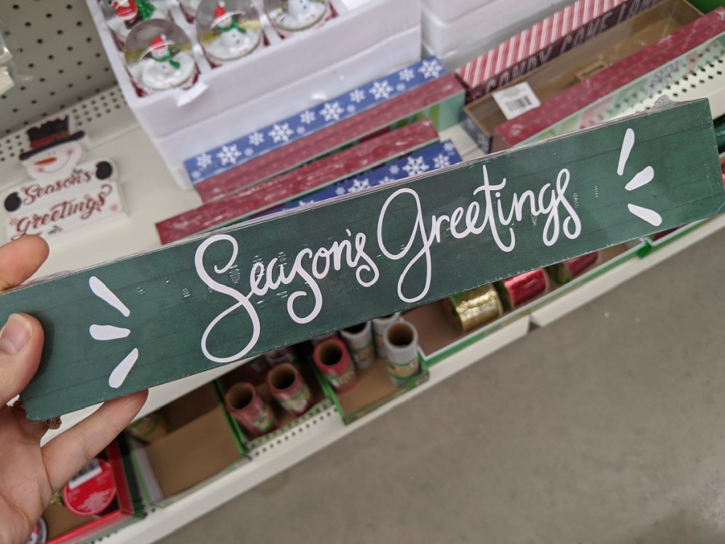 hand holding green sign that says Seasons Greetings on it