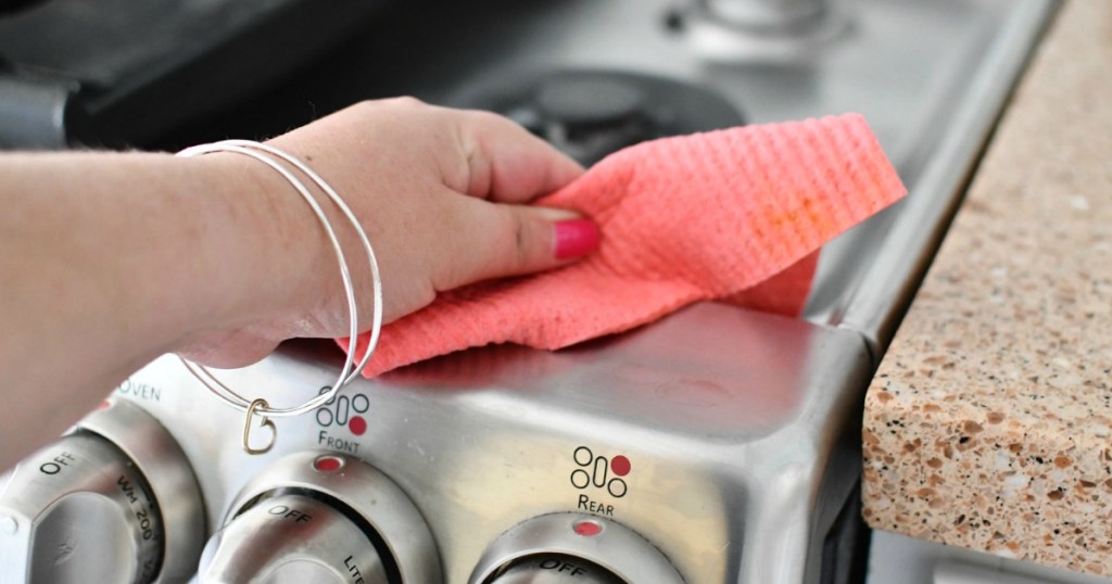 hand holding sustainable products and eco friendly products pink swedish dishcloth wiping stove top