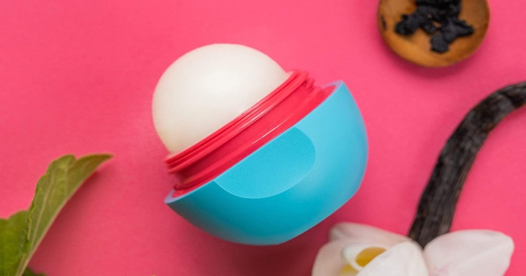 eos lip balm with the lid off, laying on a pink background with vanilla and mint nearby.