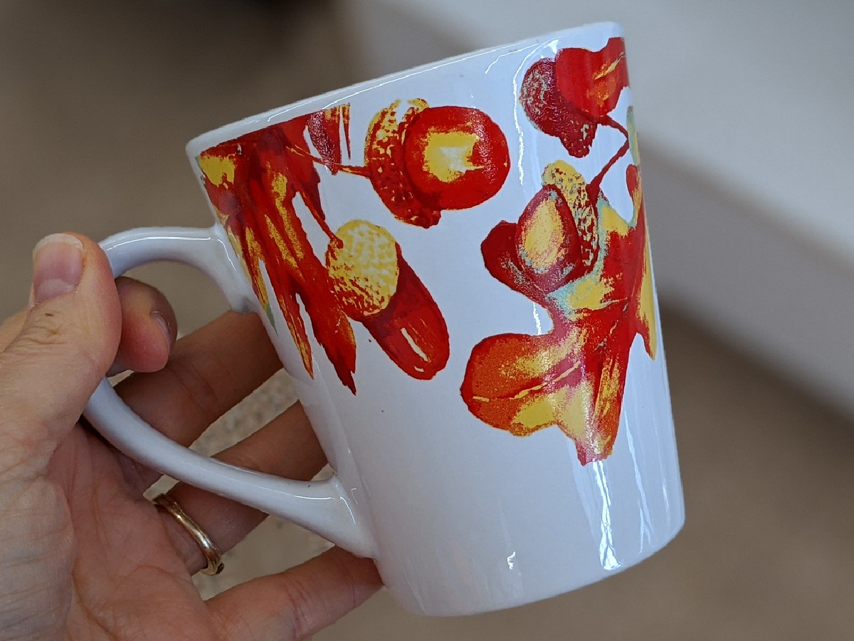 hand holding mug that has leaves painted on it