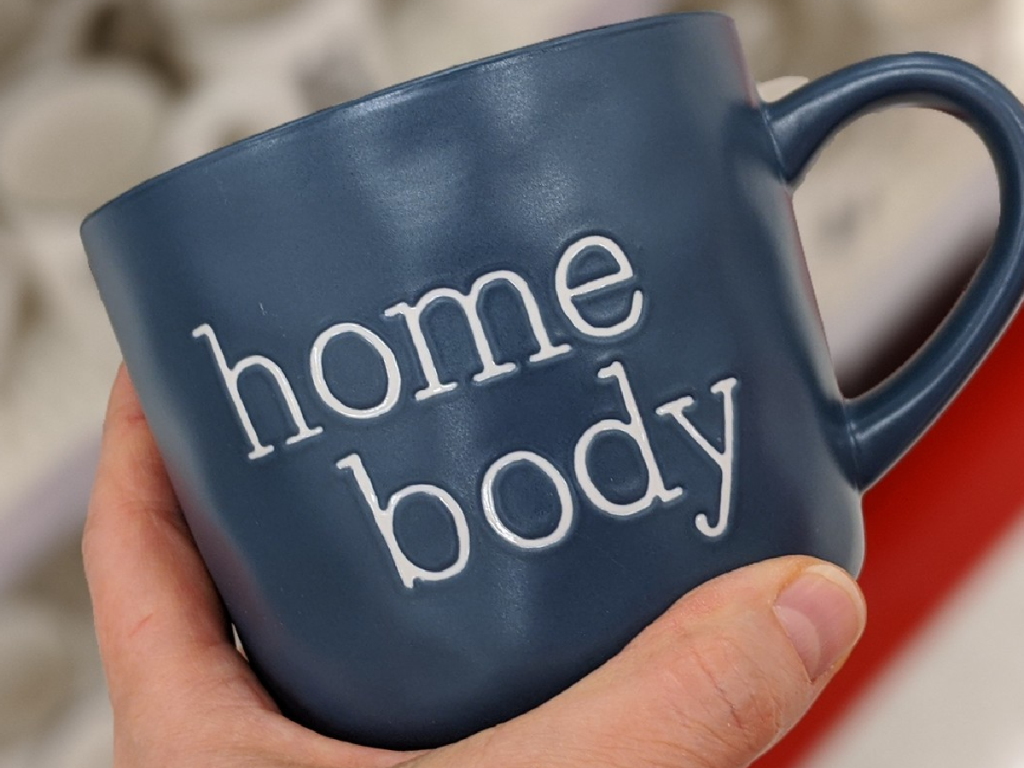 hand holding blue mug that says "home body" on it