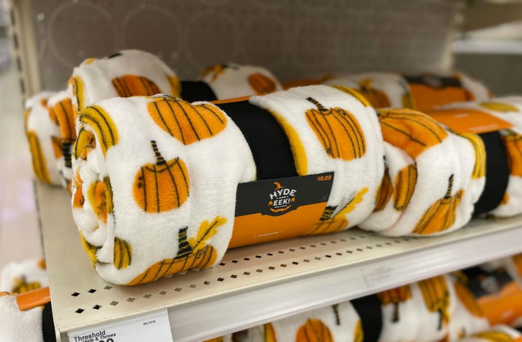 cream colored throw blanket with orange pumpkin print on a store shelf