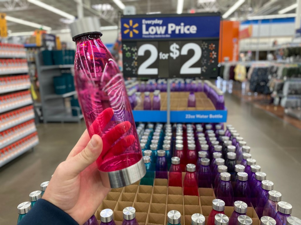 hand holding up pink water bottle by store display with price
