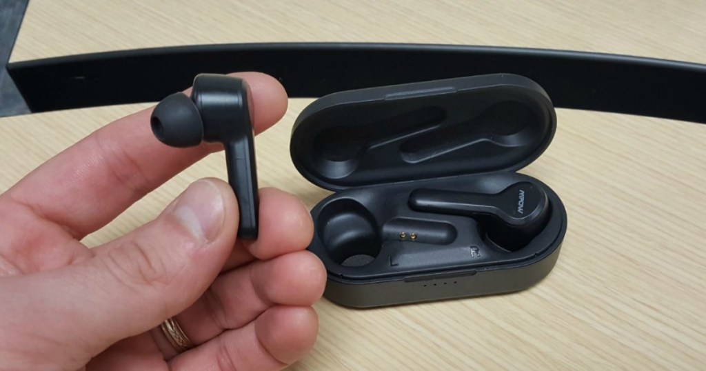 man holdig earbud in front of charging case