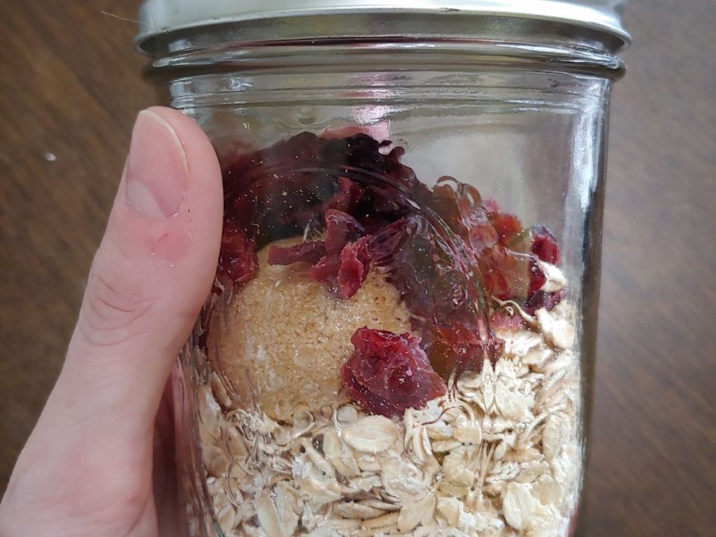 hand holding mason jar filled with craisins oats and brown sugar
