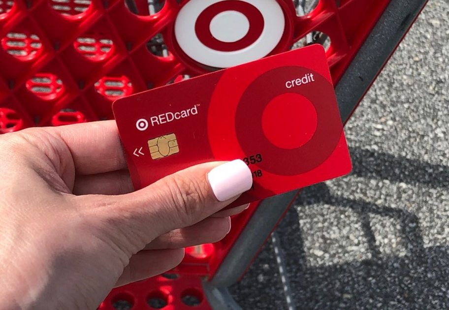 woman's hand holding a target redcard above a target shopping cart